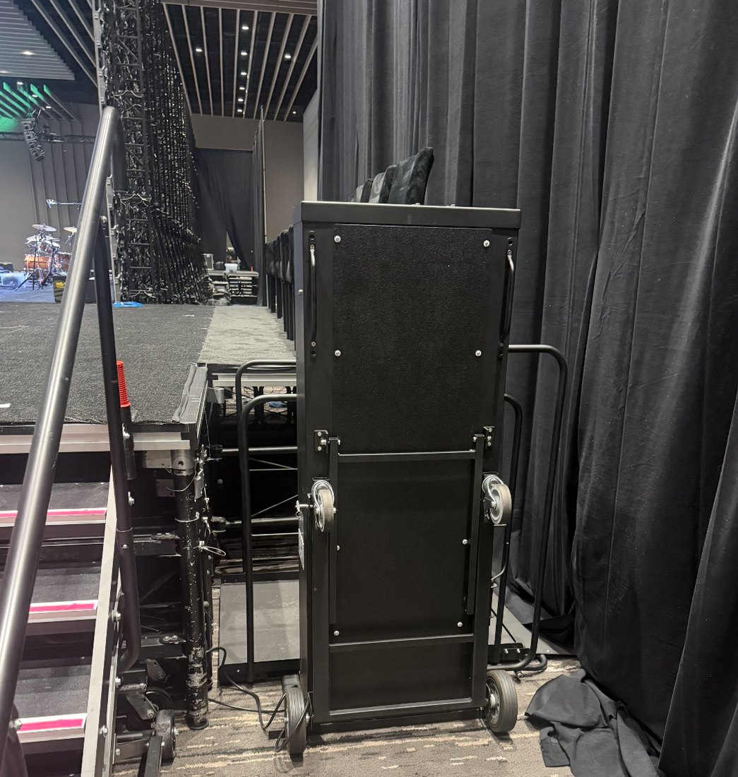 A portable stage lift positioned beside the stage deck, finished in black to blend with the stage skirt and drape